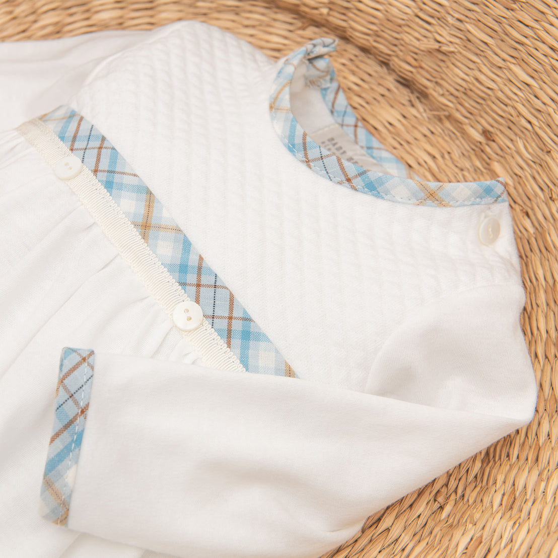 White Mason Newborn Gift Set with plaid blue and beige accents on a wicker background, ideal for a christening. The garment has snap buttons for easy dressing.