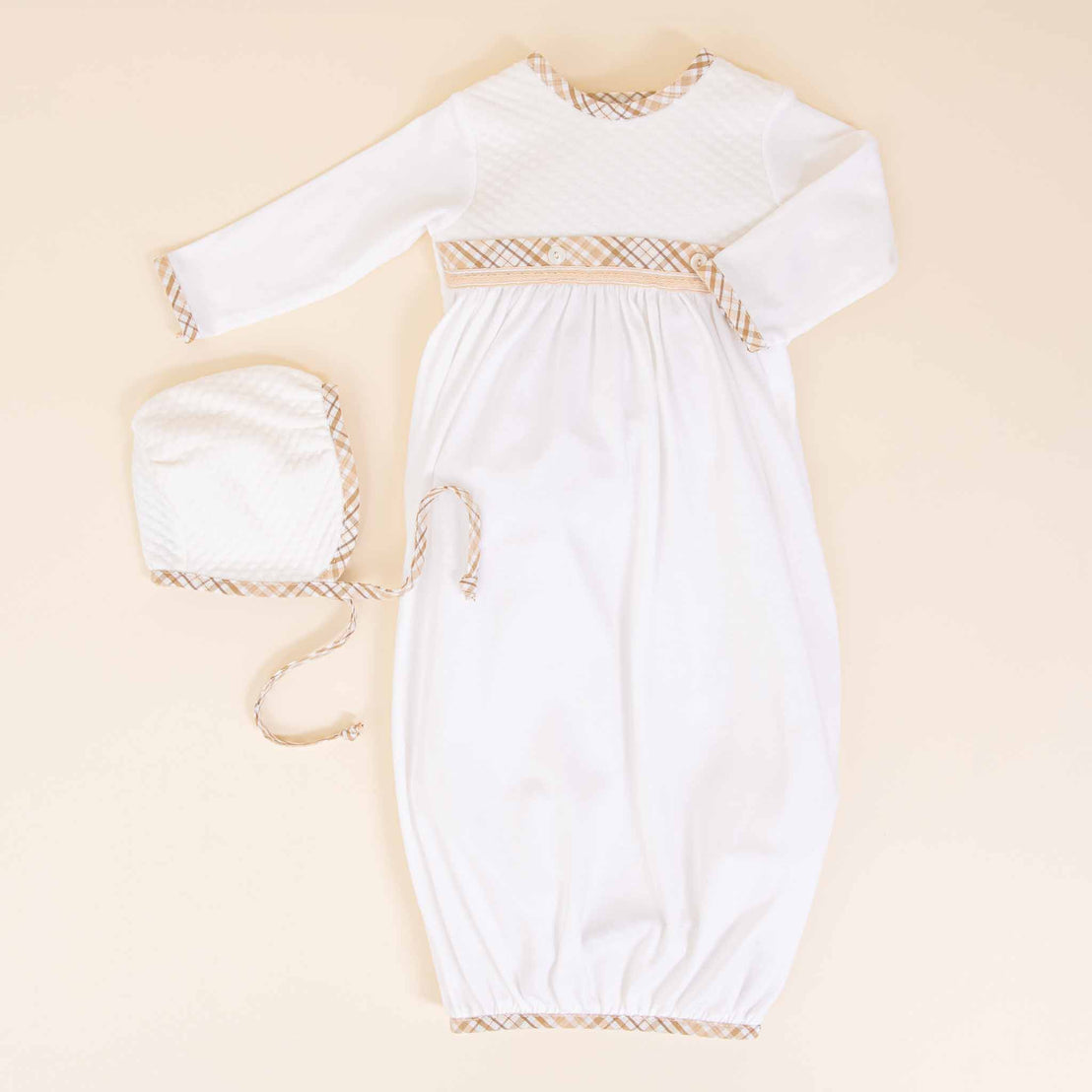Dylan Newborn Gift Set christening garments with delicate beige patterns on a collar, waistband, and cuffs, paired with a matching bonnet, displayed on a soft beige background.