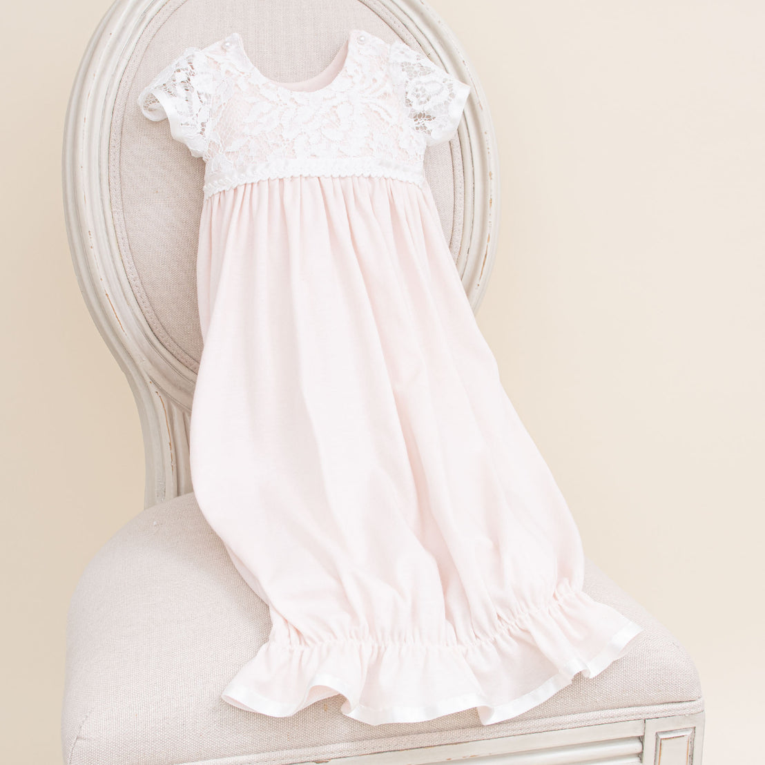 A delicate Rose Newborn Layette displayed on an upscale vintage chair with ornate details.