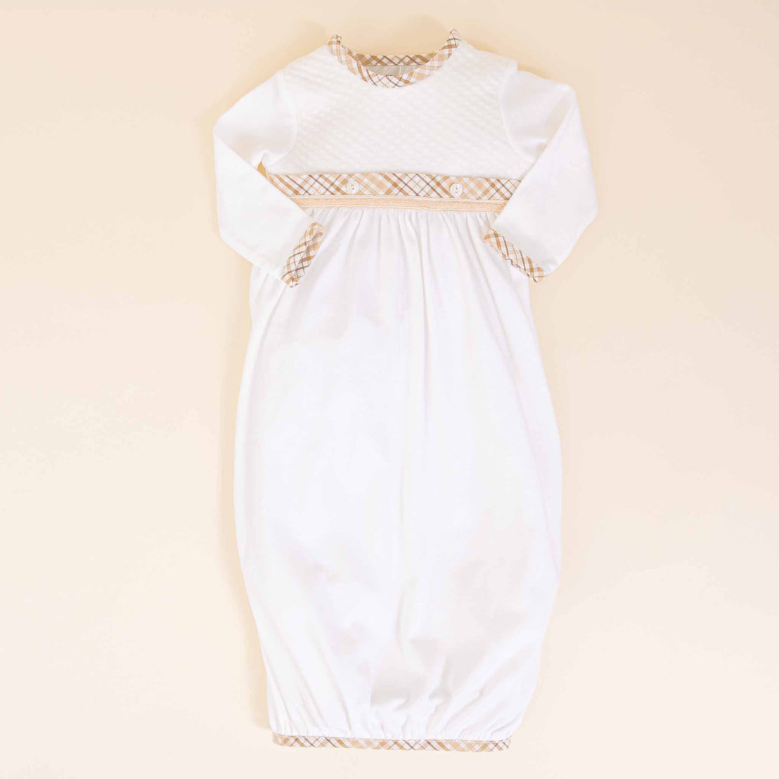 A white Dylan Layette with detailed golden embroidery across the chest and sleeves, laid flat on a soft beige background, perfect as a coming home outfit.