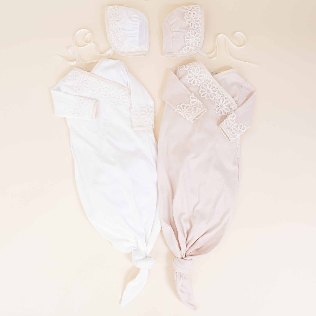 Sentence with product name: Two Hannah Newborn Gift Sets, displayed symmetrically on hangers, featuring delicate lace details and heirloom qualities, with one outfit in white and the other in soft pink, perfect as a coming.