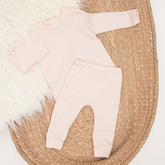 Ava Pima Top & Leggings outfit consisting of a blush pink pima cotton long-sleeved shirt and matching leggings, displayed flat on a woven basket with a fluffy white rug in the background.