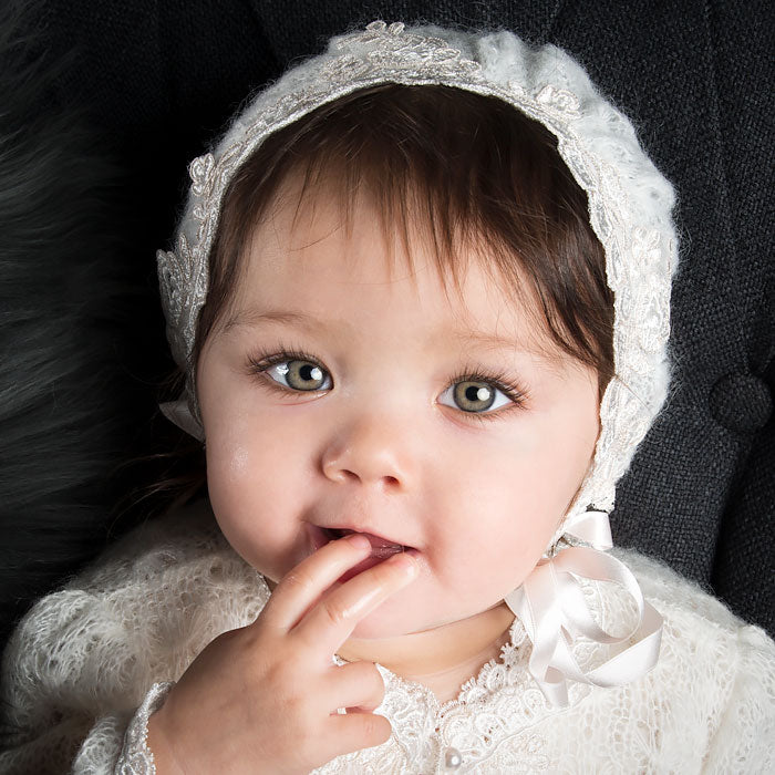 Baby girl with finger in mouth looking at camera wearing the Penelope knit baby girl bonnet.