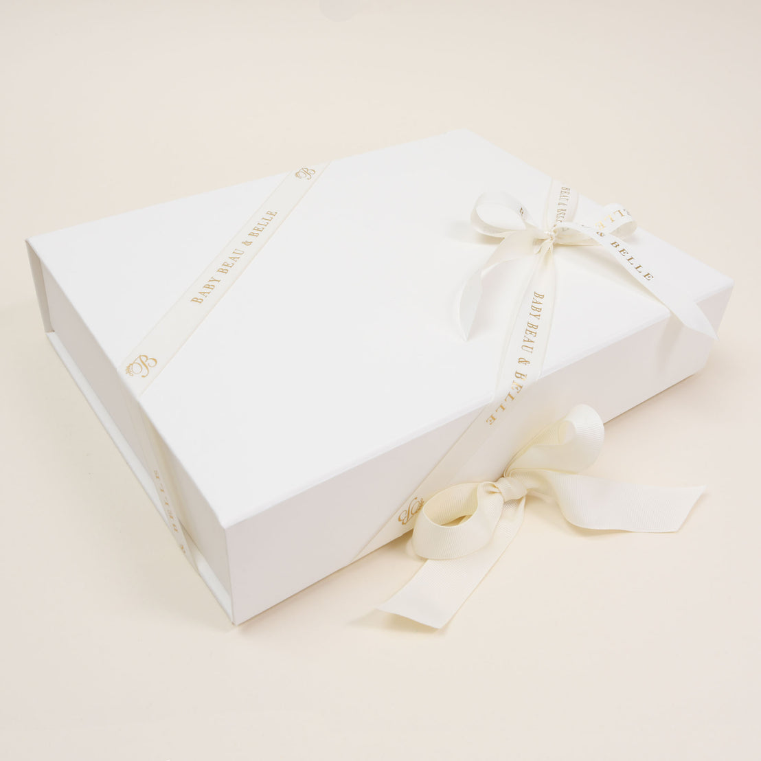 An elegant Baby Beau & Belle white gift box with a magnetic closure, tied with a delicate ivory ribbon, showcasing a sophisticated and minimalist design on a soft beige background.