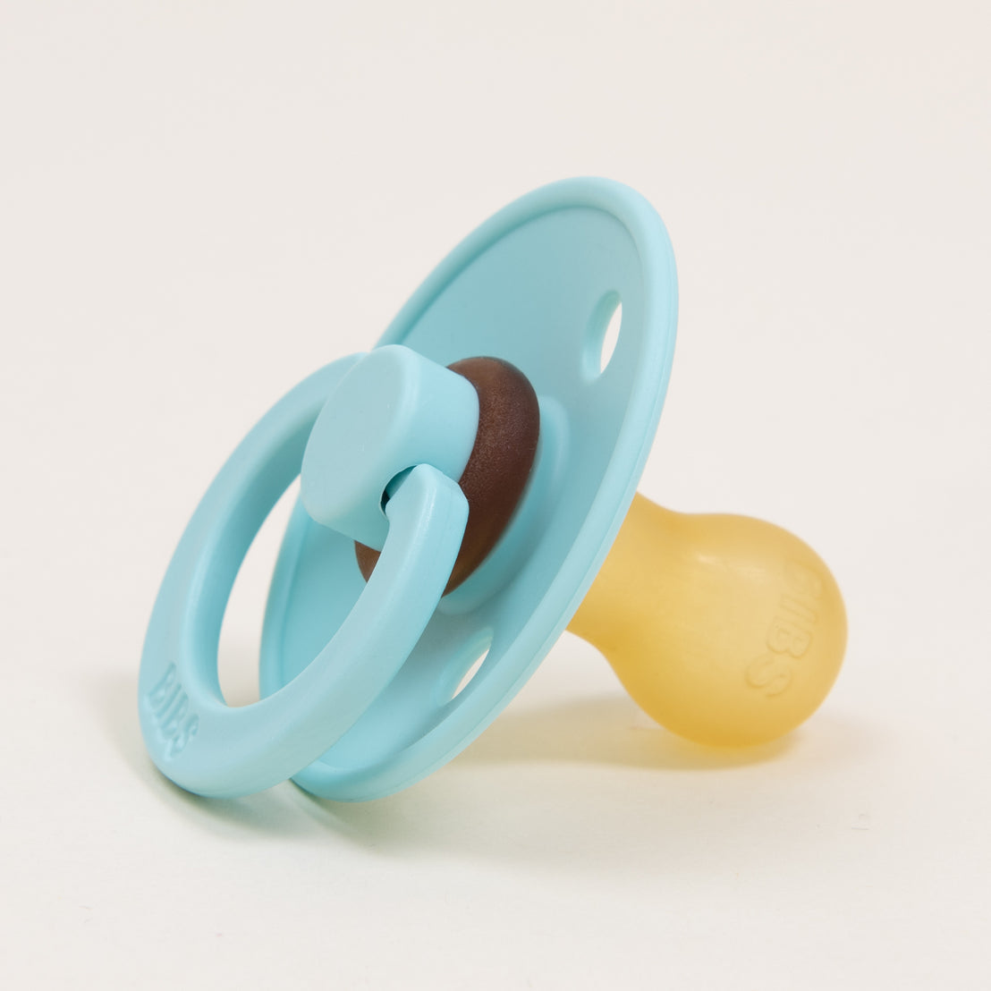 A mint Bibs pacifier with a yellow nipple, designed in Denmark, resting on a white background. The handle has the word "Bibs" embossed on it.