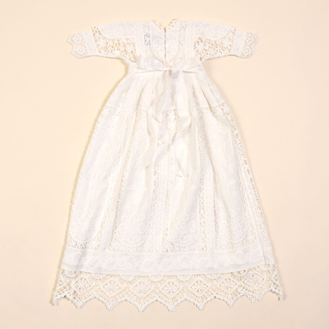 A vintage Adeline Newborn Lace Dress or Gown with short sleeves and intricate patterns displayed against a cream background.