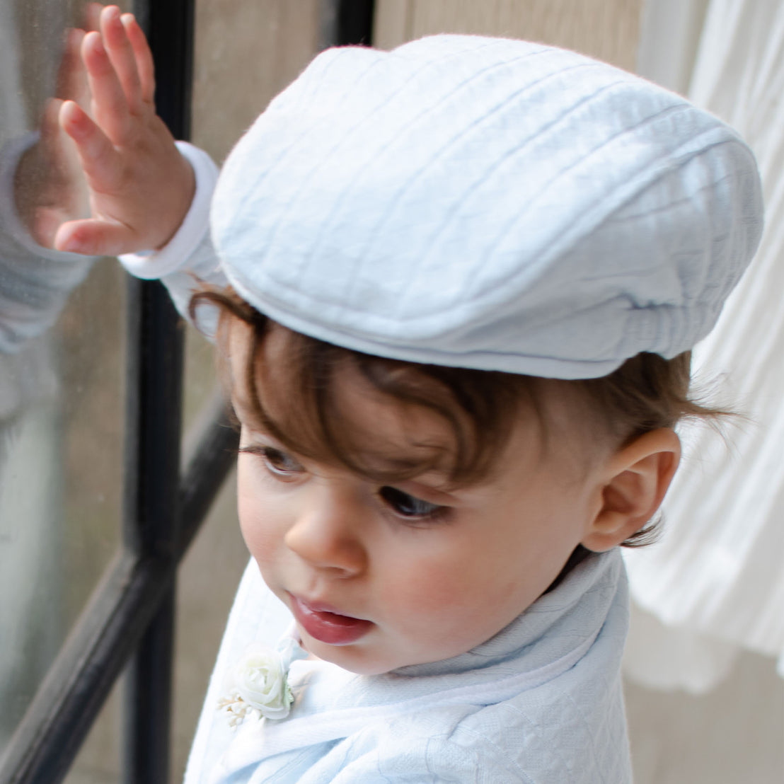 Baby boy looking outside a window and wearing the Logan Newsboy Cap. 