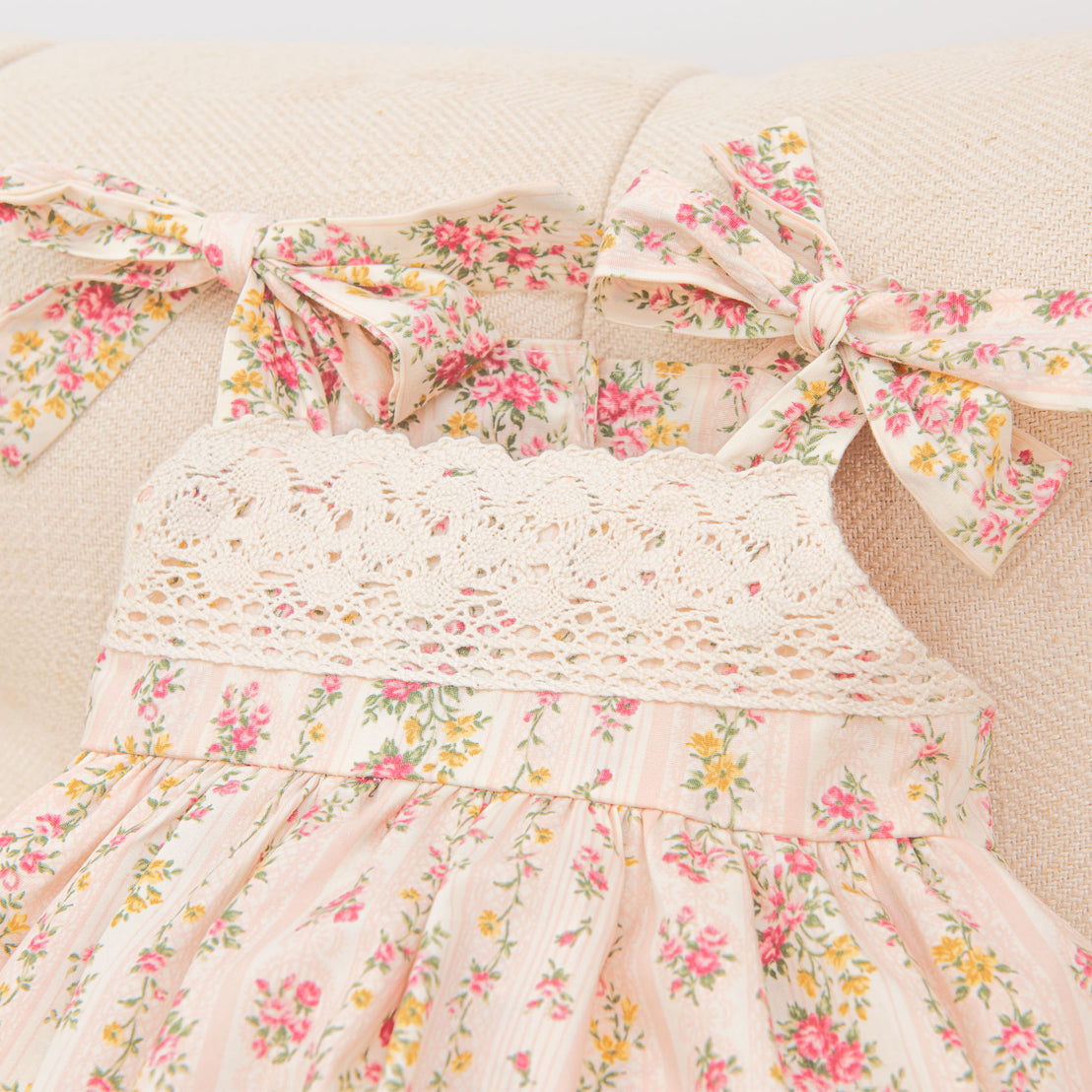 Flat lay of the Eloise Romper Dress in the "Blush" color. Details show the rose floral patterns and tie shoulder straps.