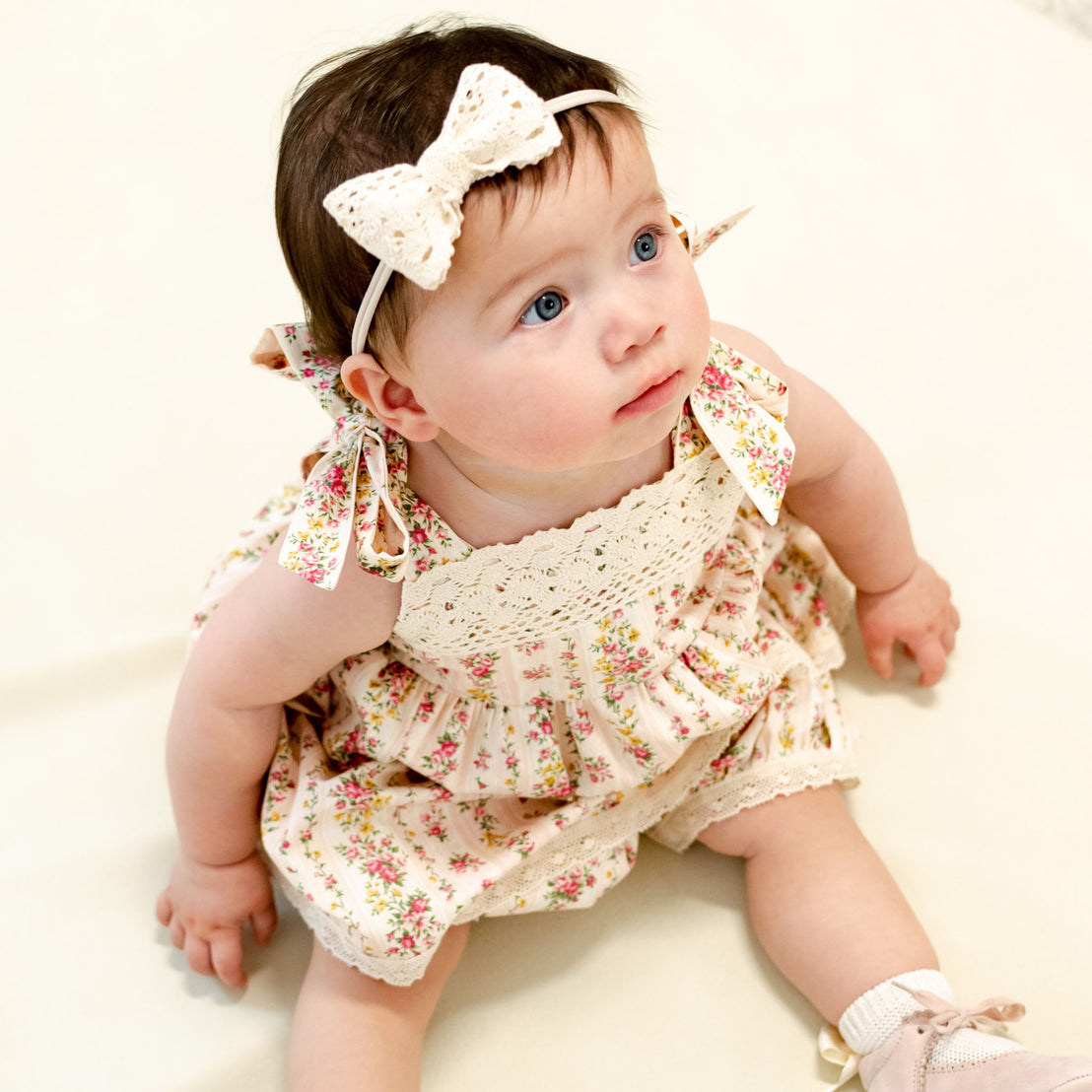 Baby girl wearing the "Blush" Eloise Romper Dress with matching Eloise Bow Headband.