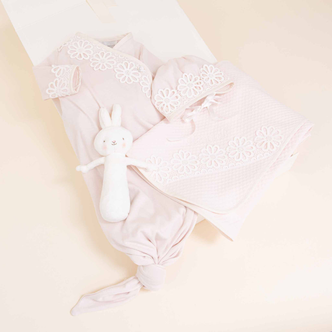 A collection of Hannah Newborn Gift Set items including a pink blanket, a onesie, and a soft white bunny toy, all arranged neatly inside an open white box against a pastel background by Baby Beau & Belle.