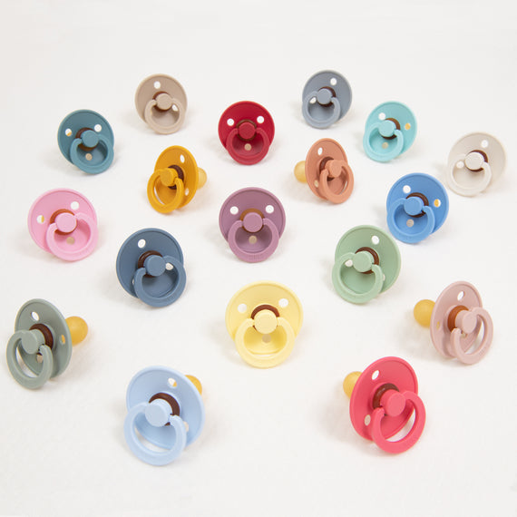 An assortment of colorful Bibs Pacifiers designed in Denmark, arranged in a grid on a white background, each featuring a unique combination of pastel shades.