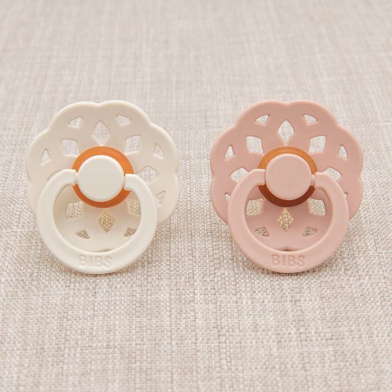 Two bibs baby pacifiers - one in ivory and one in blush.