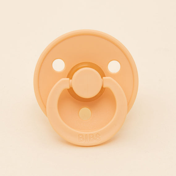 A Bibs pacifier 2 pack in Peach Sunset with a round shield and two air holes, prominently featuring the brand name "bibs" on the button.