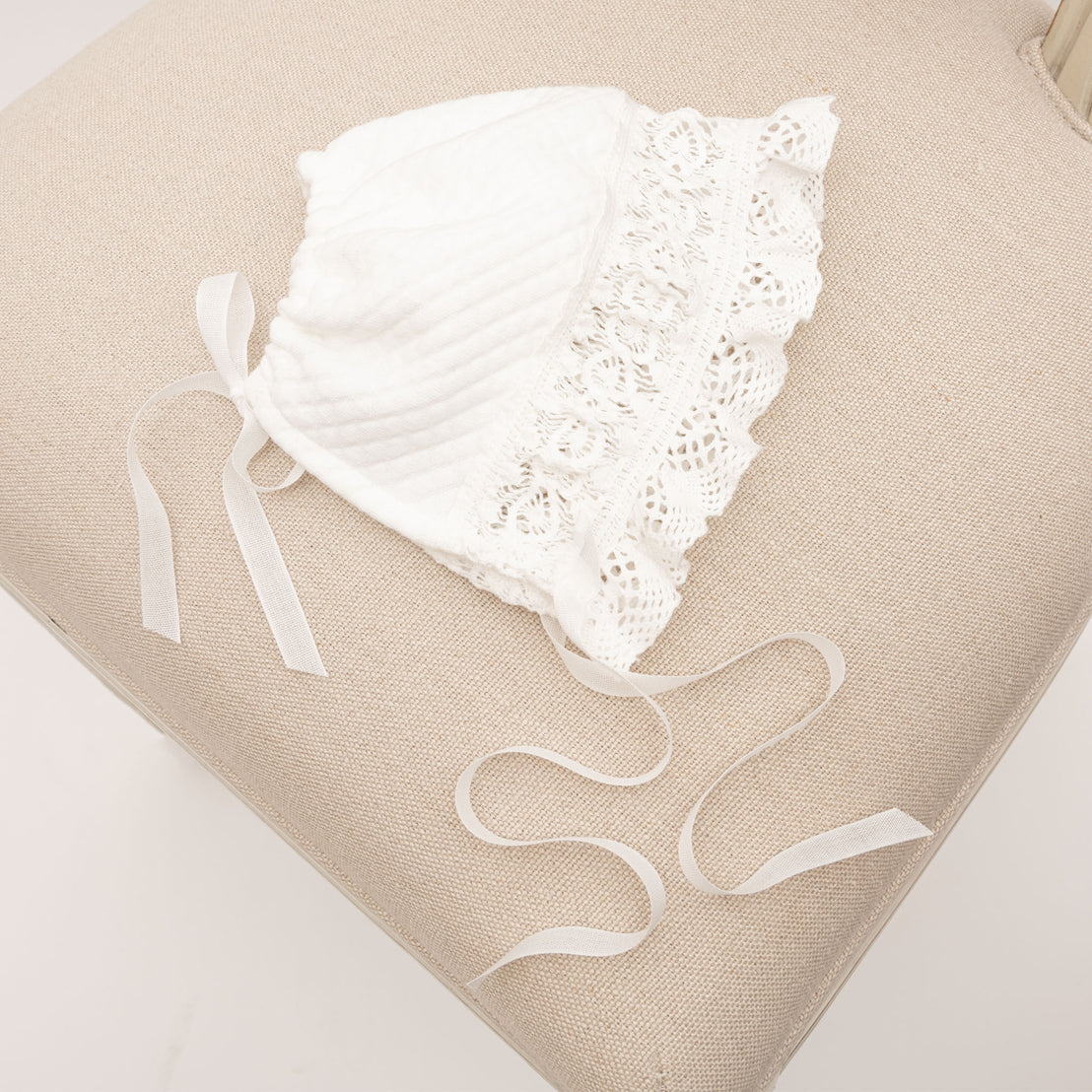 Flat lay of the Lily Quilted Cotton Bonnet showcasing the details of the soft stretch lace trim in light ivory and ruffle detail