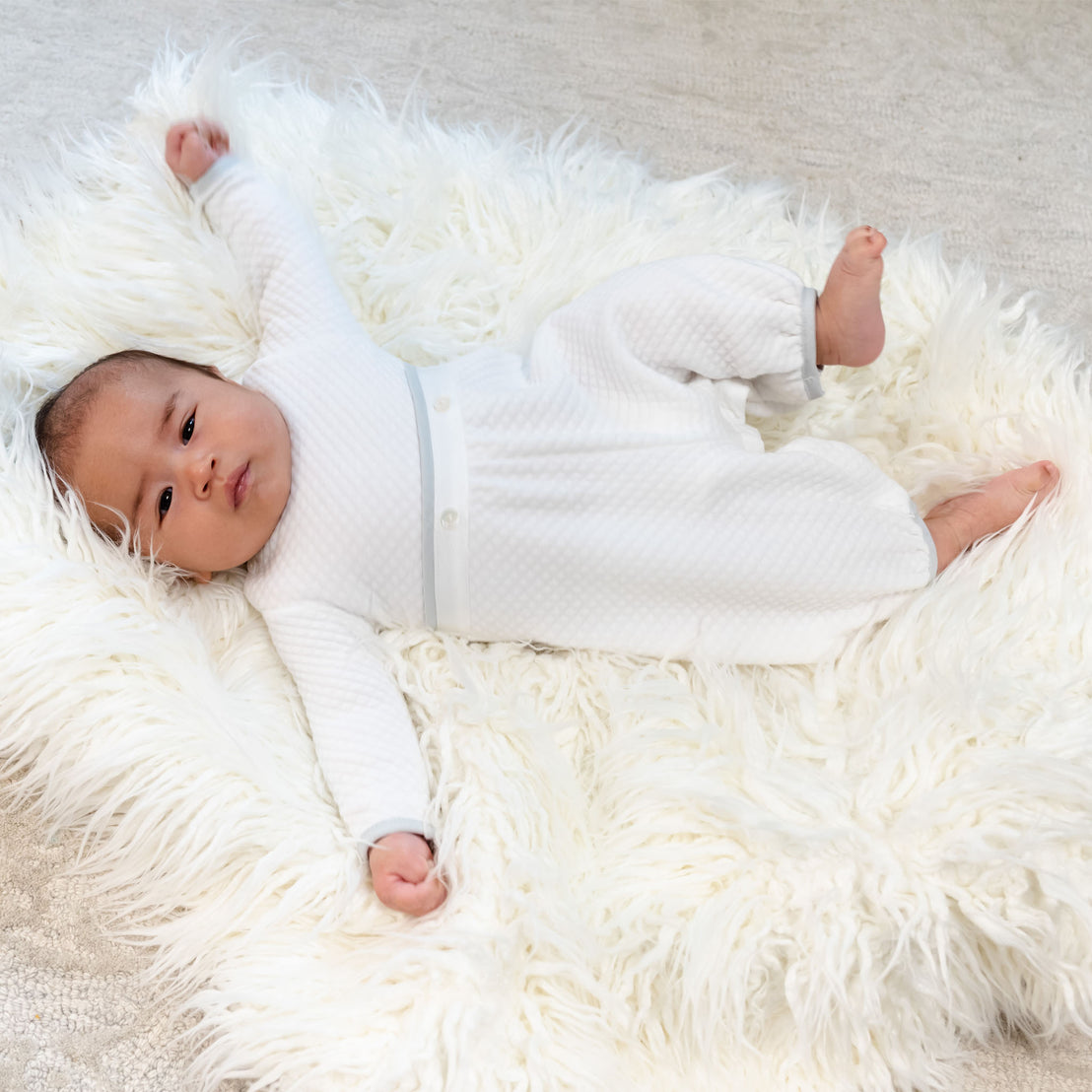 Baby boy laying sideways on a rug wearing his quilted cotton newborn romper. 