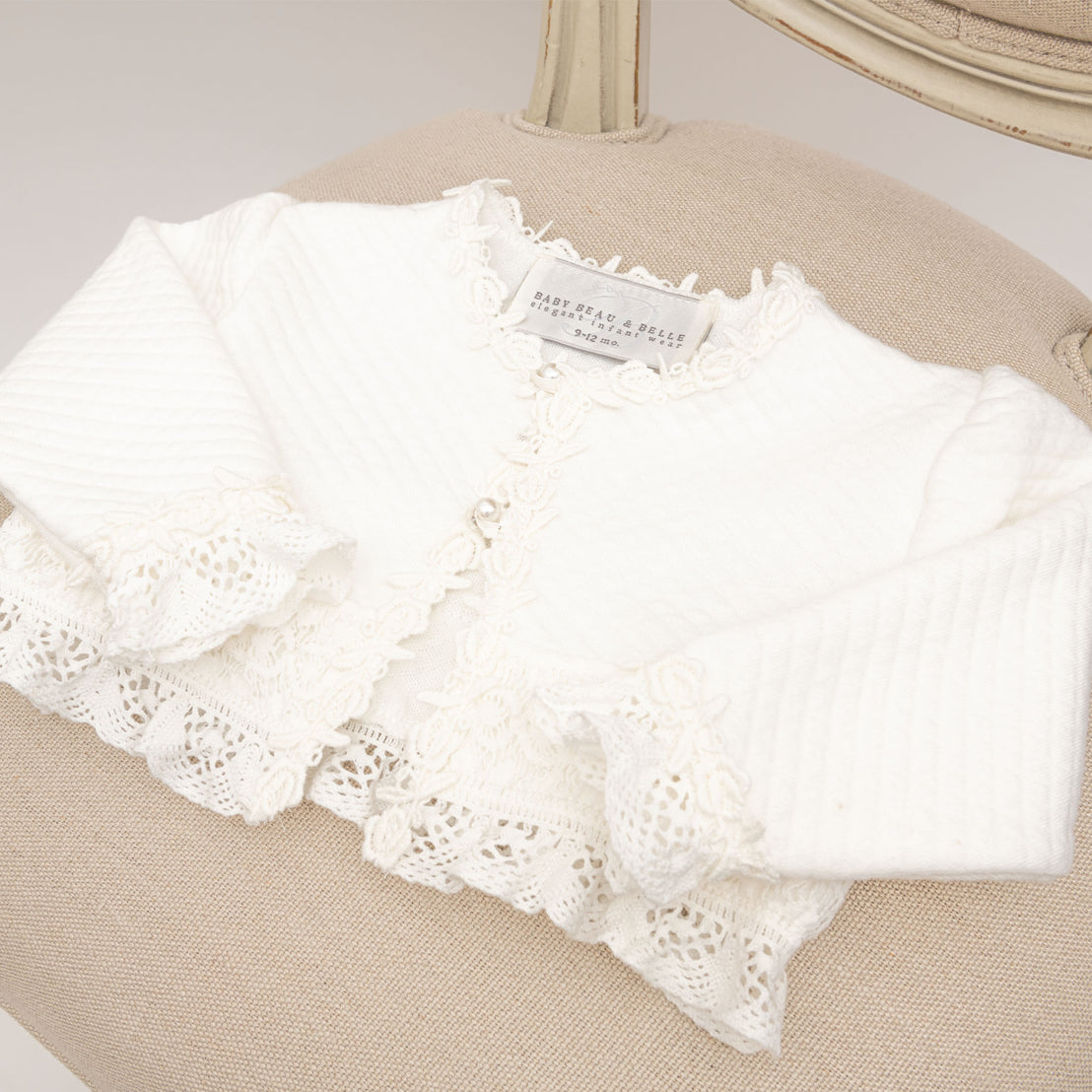 Flat lay of Lily Quilted Cotton Sweater made with ivory quilted cotton, ivory cotton lace with rose and vine floral embroidery, light ivory stretch lace, and pearl style buttons 