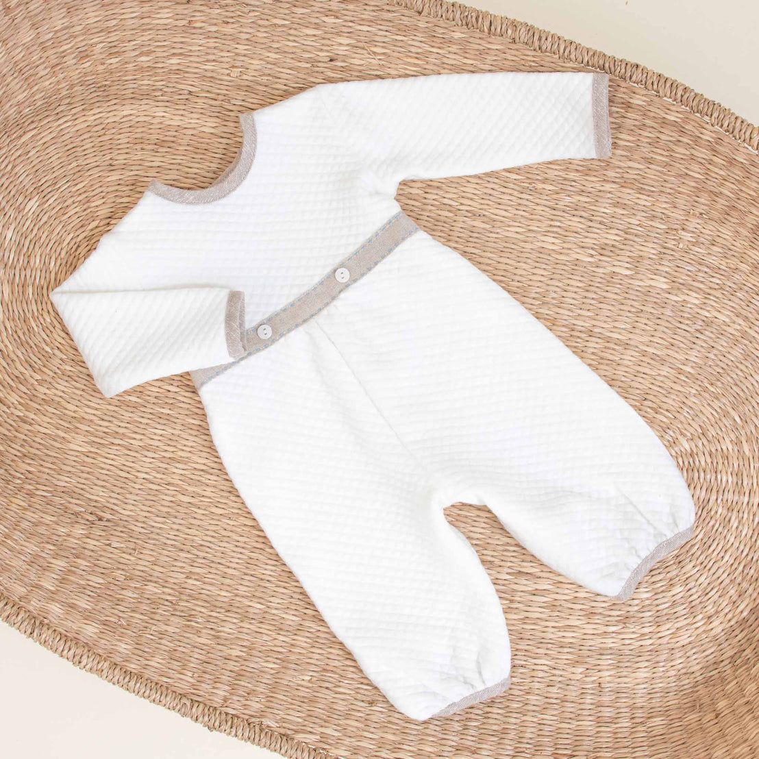 An upscale Austin Newborn Romper with long sleeves and a gray trim, displayed flat on a round woven wicker mat against a beige background.