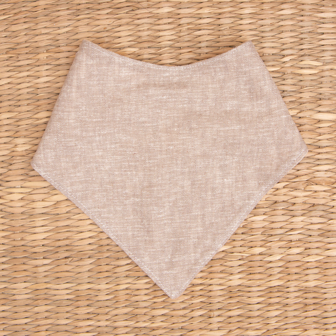 Flat lay photo of the sand colored Silas Bandana Bib in a woven basket