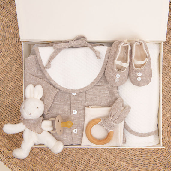 Photo of the tan colored Silas Gift Set in a Gift Box. Included in the box is the shirt, pants, booties, bib, teether, bunny, pacifier, and personalized blanket.