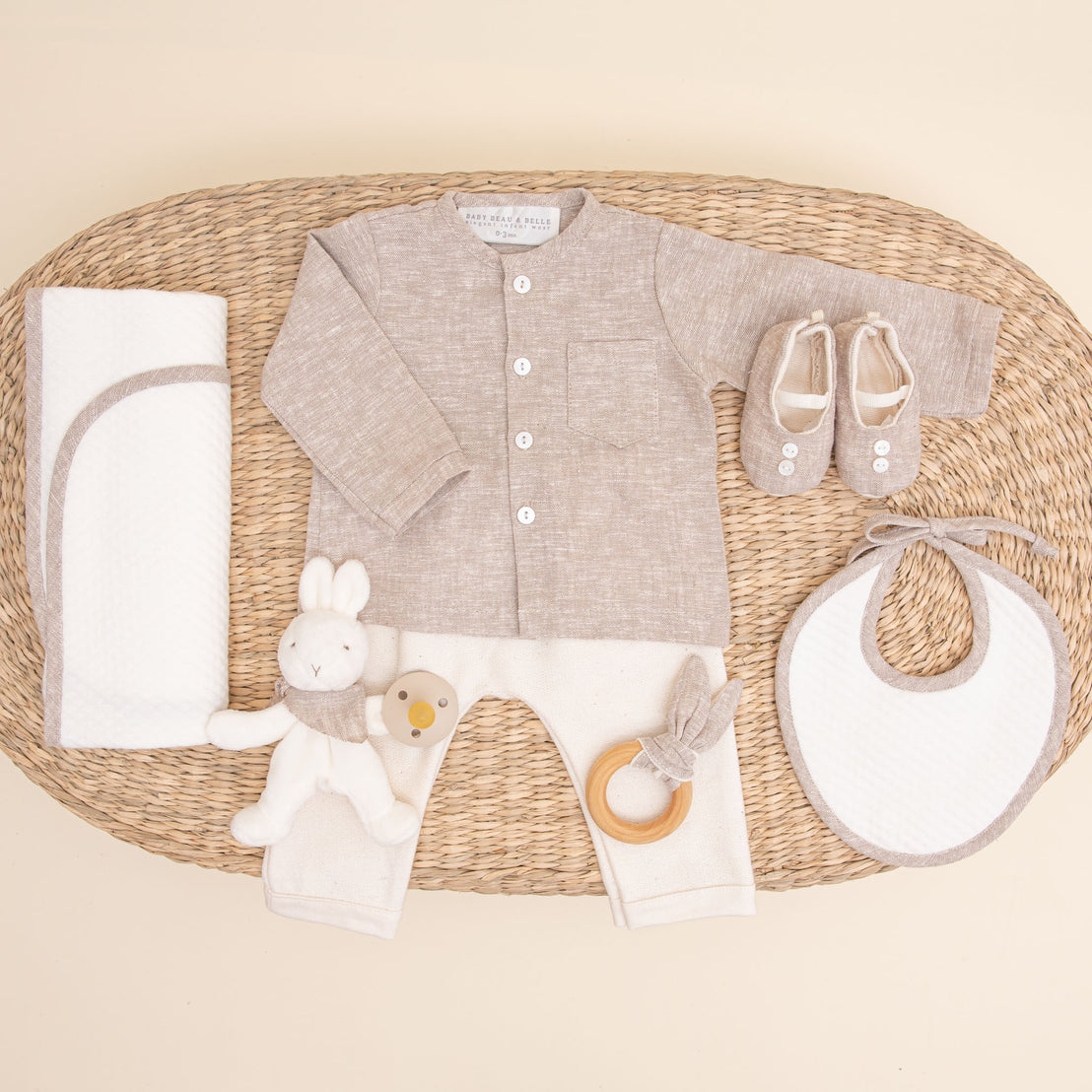 Flat lay photo of the sand colored Silas Gift Set. Included in the photo is the shirt, pants, booties, bib, teether, bunny, pacifier, and personalized blanket.