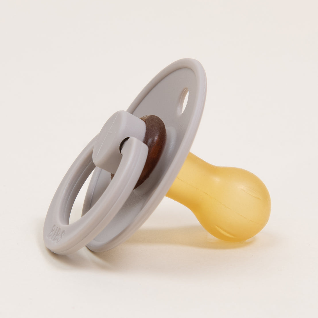 A Bibs Pacifier in Sand with a sand-colored handle and a yellow nipple on a white background.