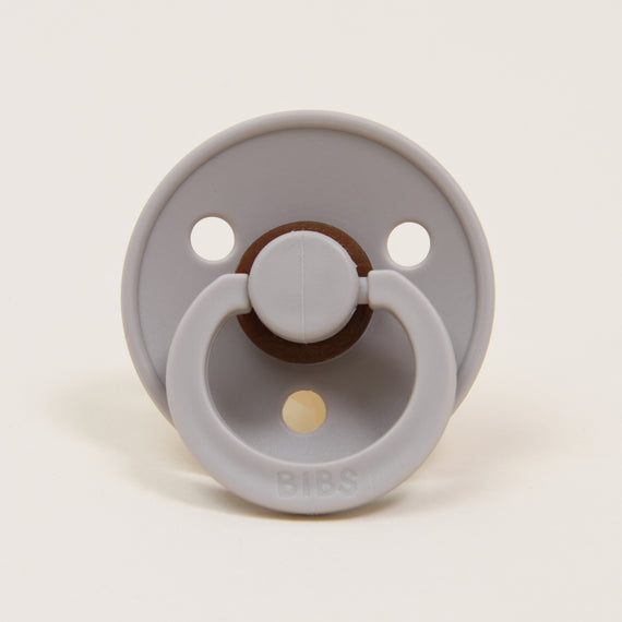 A Bibs Pacifier in Sand featuring an upscale design with two air holes and a natural brown button handle, set against a plain white background. Perfect as a baby gift.