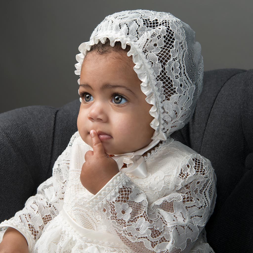 Baby girl with finger on mouth wearing the long sleeve Victoria Christening Gown.