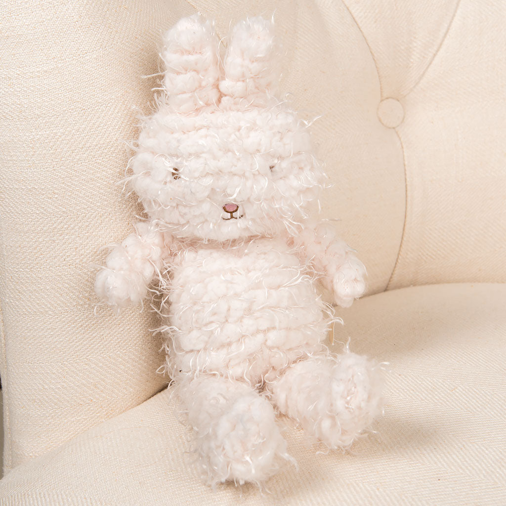 A fluffy, textured Shaggy Hoppy Bunny plush toy sitting on a cream-colored sofa. The bunny has a visible smile and is in a seated position.