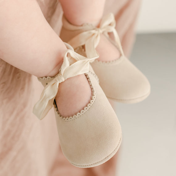 Close-up of a child's feet wearing Kristina Tie Mary Janes with satin ribbons, against a soft pink fabric background, perfect for baptism and vintage-inspired heirloom photography.