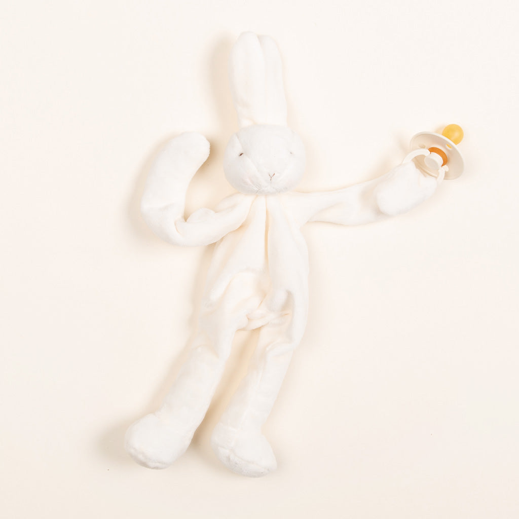 A Silly Bunny Buddy pacifier holder with long ears and limbs, perfect for a baptism, on a pale cream background.