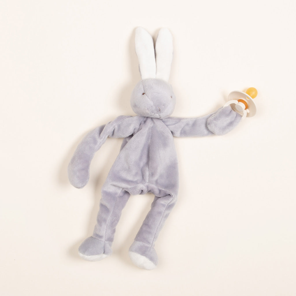 A Silly Bunny Buddy in pale blue with long ears and limbs, lying on a light background. The bunny holds a yellow and white pacifier holder, perfect for an upscale baptism gift.