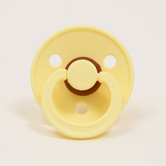 A yellow Bibs Pacifier in Sunshine color with a brown button detail, branded "bibs".