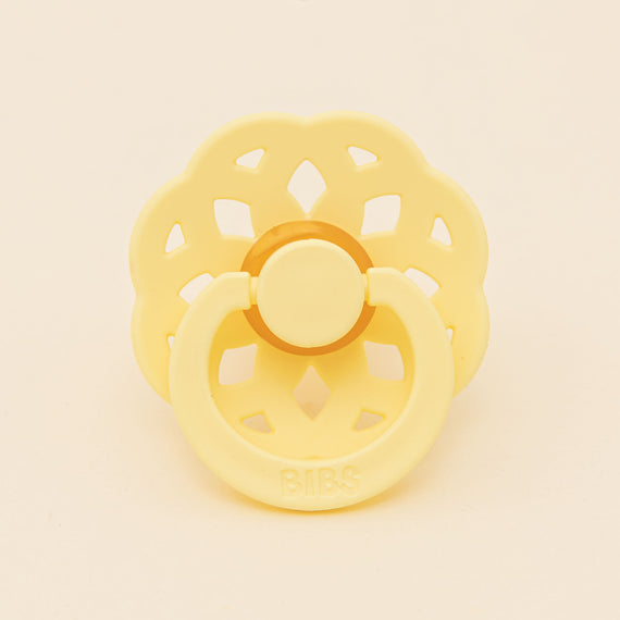 A yellow Bibs Lace pacifier with a flower-shaped shield and handle, set against a neutral background. The brand "bibs" is embossed on the front.