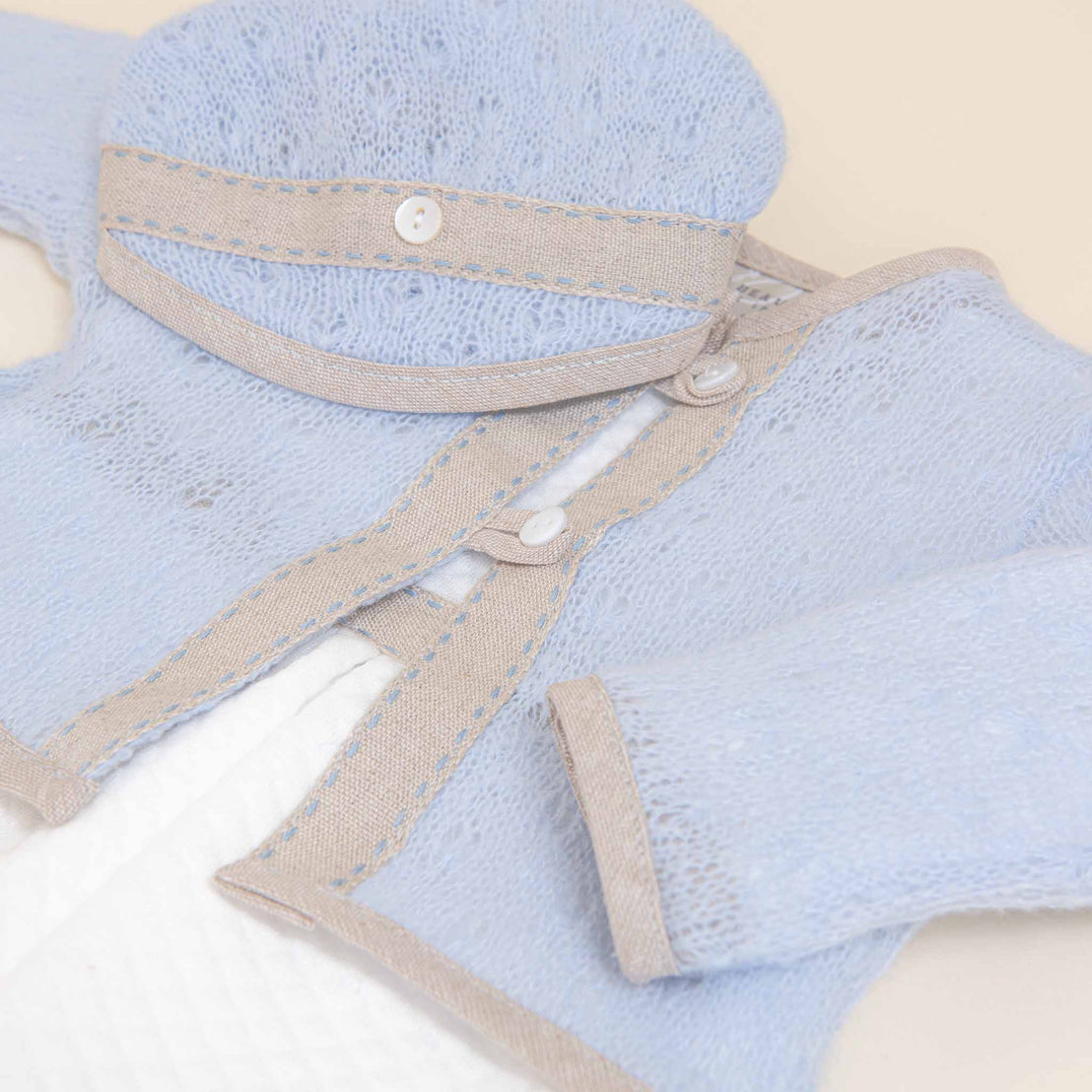 A close-up image of a baby's Austin Sweater with a beige trim and intricate fabric details, showcasing buttons and textures.