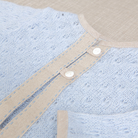 Close-up of an Austin Sweater featuring a pale blue heirloom lace detail next to a beige fabric with small white buttons.