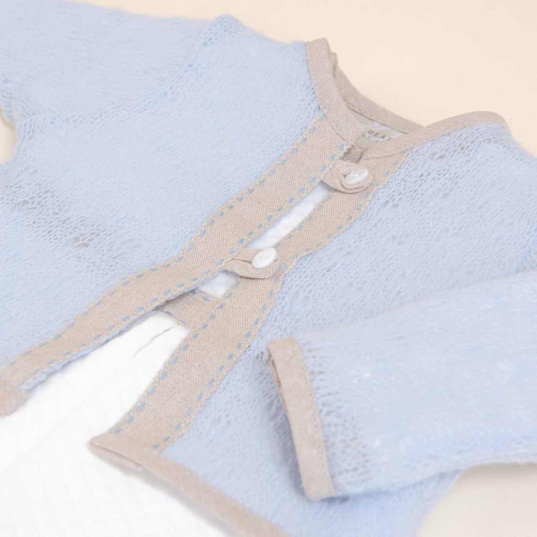 A close-up image of a light blue, knitted Austin Sweater with delicate button details and a soft beige trim, displayed on a plain background.