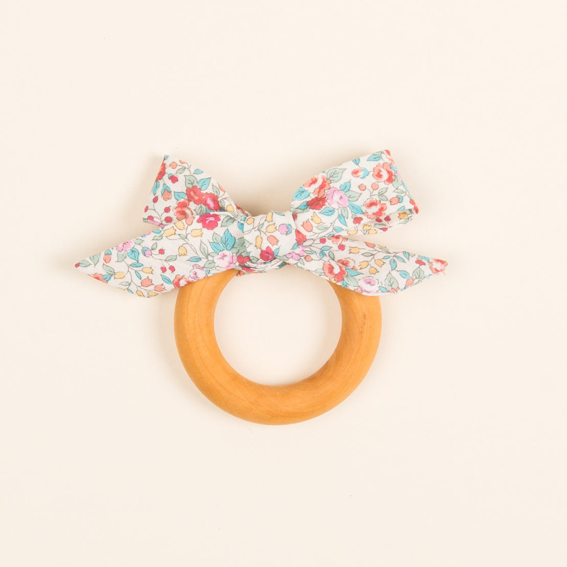 An upscale, vintage-inspired Petite Fleur Wooden Teether Ring with a floral patterned fabric bow, positioned on a light beige background.