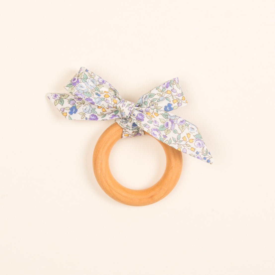 An heirloom, handcrafted Petite Fleur Wooden Teether Ring with a floral fabric bow attached, set against a light beige background.