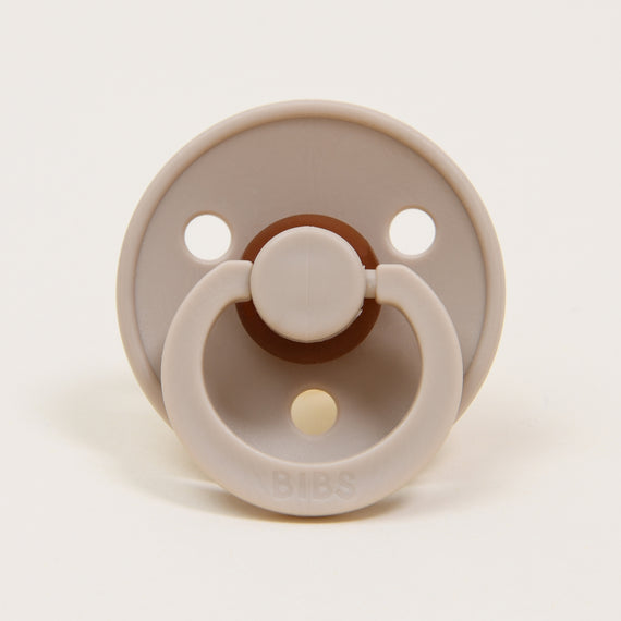 A beige Bibs Pacifier 2 Pack | Vanilla with two large air holes, featuring a brown button handle and a white ring, branded "bibs" on an upscale natural background.