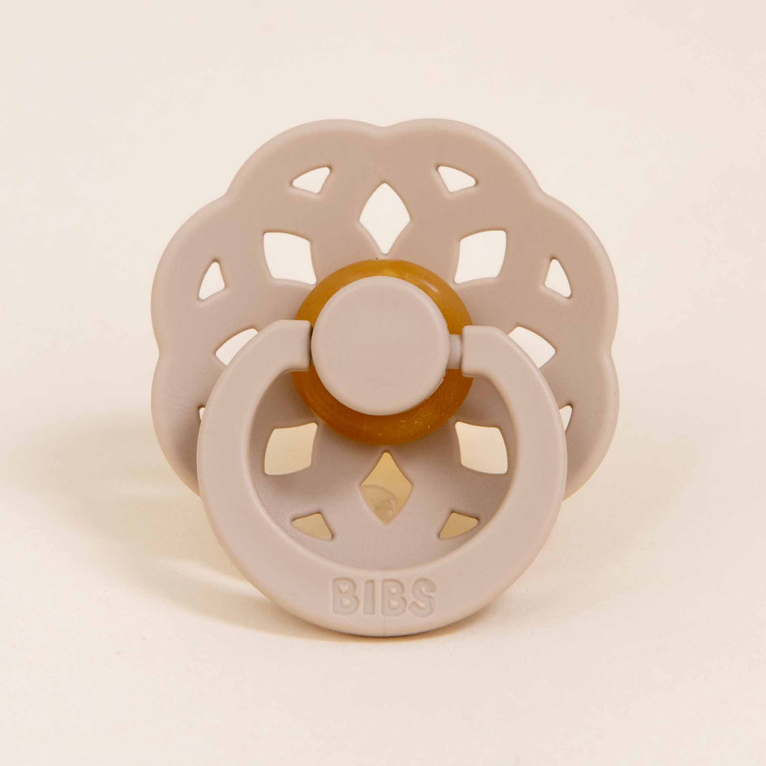 An Kristina beige pacifier with a circular, flower-shaped shield and a brown handle, displayed against a plain, light background.