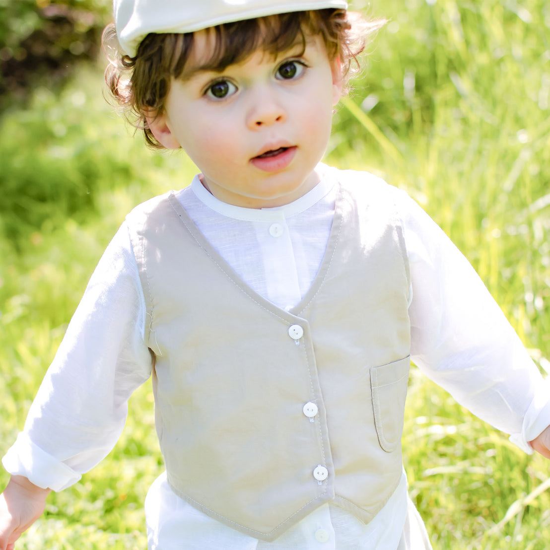 Photo of a baby boy outside in the grass wearing the Silas Vest Suit and matching newsboy cap