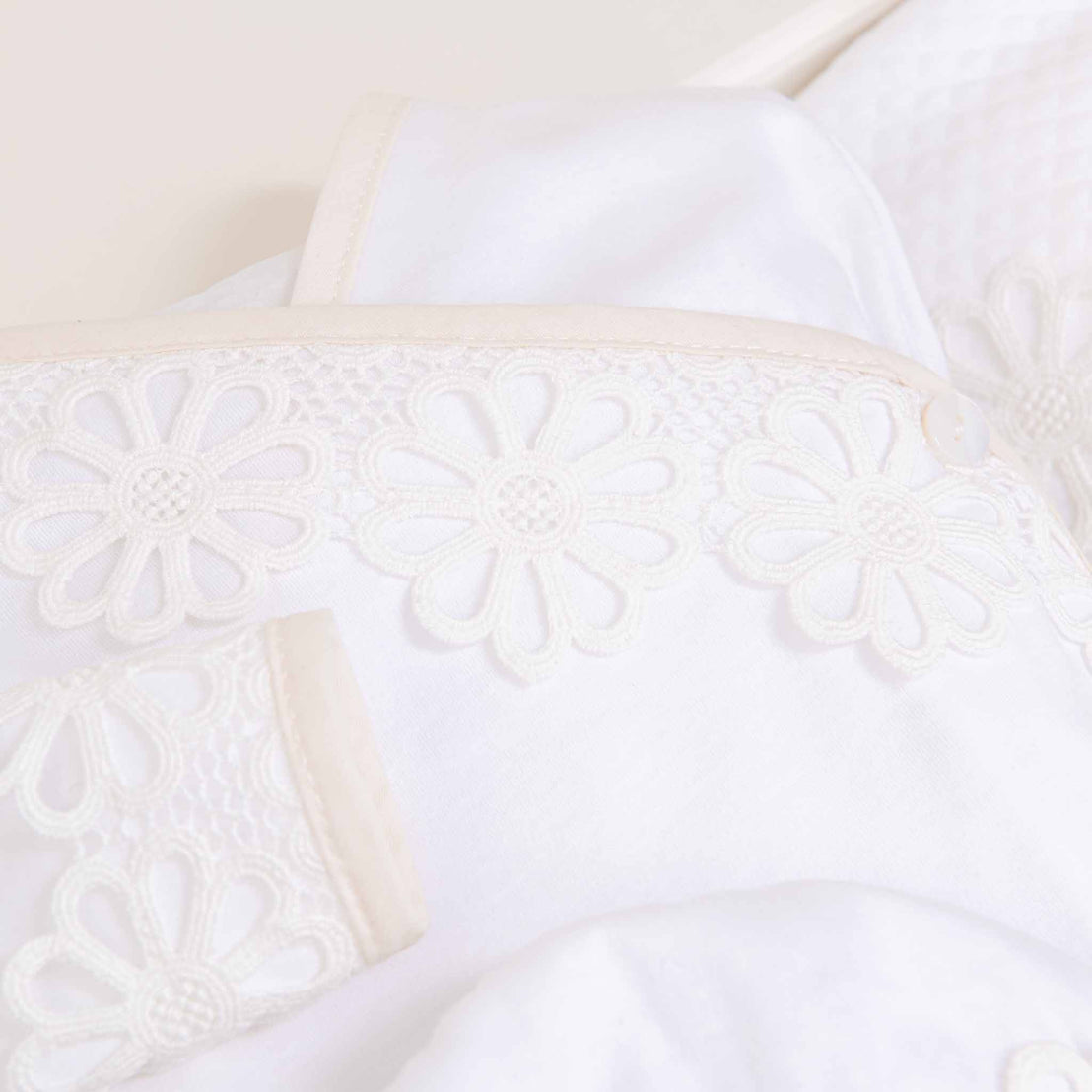 Close-up of a white pillow with intricate lace detailing featuring a floral pattern, placed on a white bedspread. Soft, gentle lighting enhances the elegant texture and design of this Hannah Knot Gown & Bonnet.