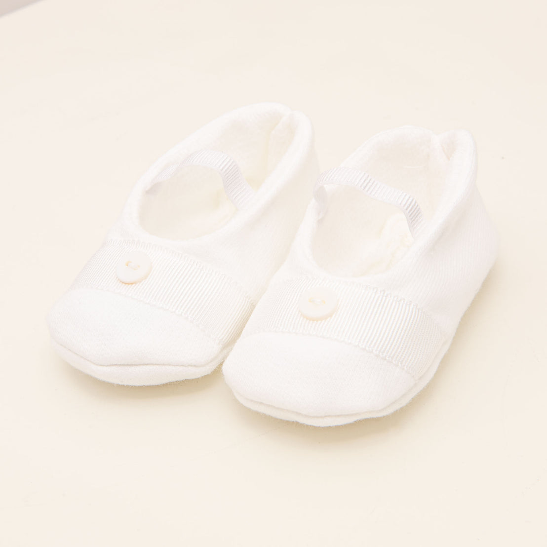 Flat lay photo of the Asher Booties made in a 100% White french terry cotton with a soft elastic strap and featuring a white grosgrain ribbon with a button detail on the top.