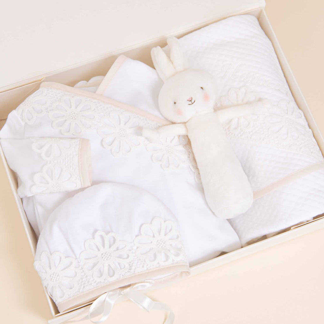 A Baby Beau & Belle Hannah Newborn Gift Set- Save 10% containing a plush bunny toy, a white blanket with floral embroidery, a coming home outfit, and a pair of booties, all neatly arranged on a soft background.