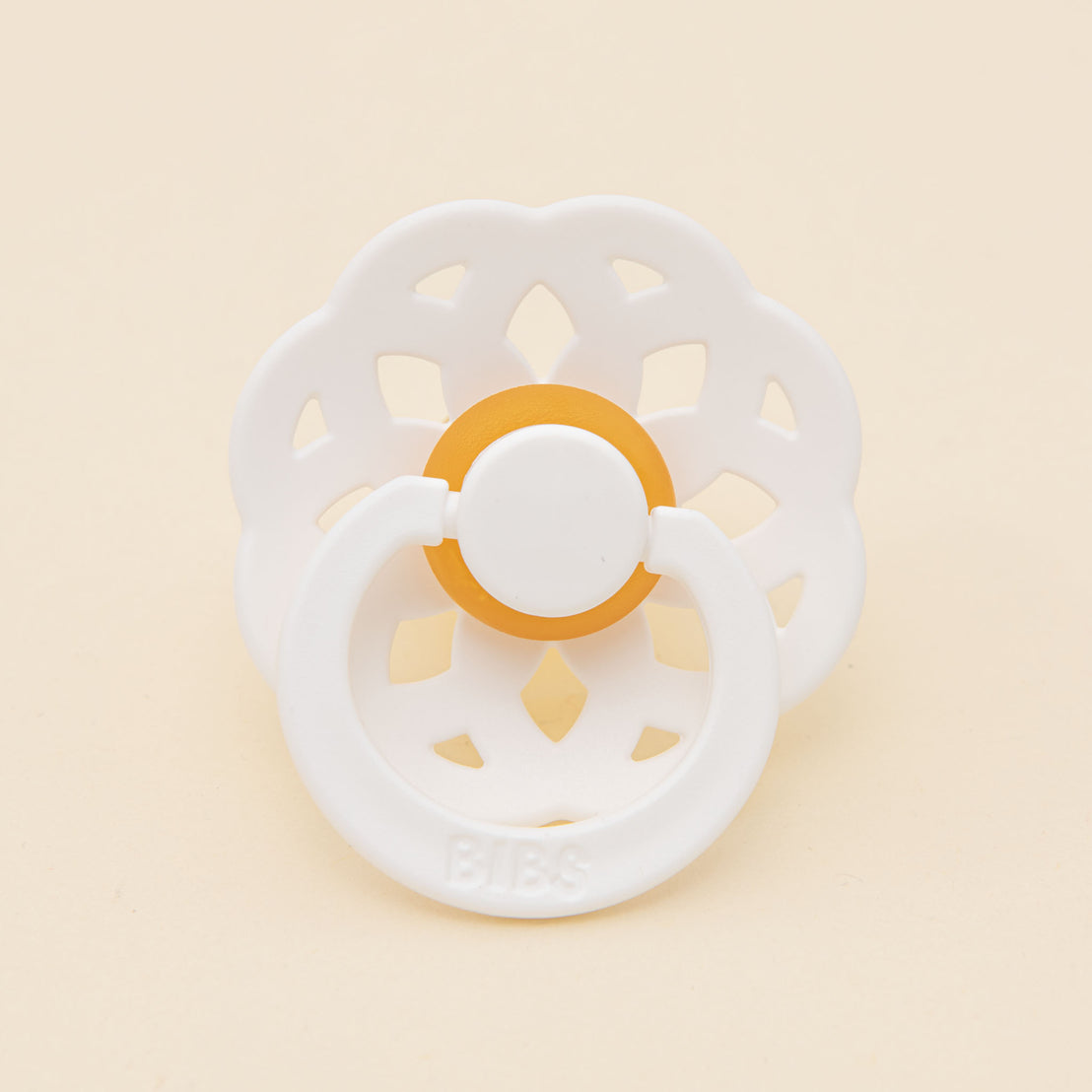 White Mila Pacifier with a round shield, featuring a delicate perforated design, resting on a pale yellow background.