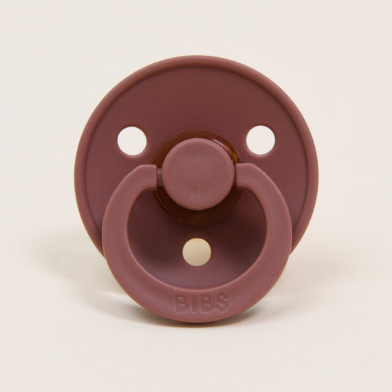 A maroon-colored Bibs Pacifier with three air holes, featuring a handle and "bibs" brand name on the button.