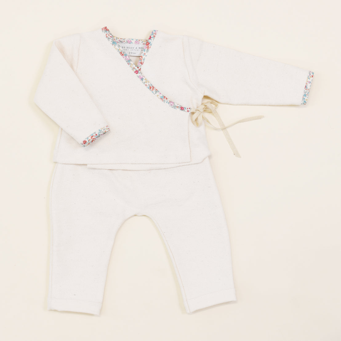 A baby's Petite Fleur Wrap Top & Pants, featuring a kimono-style top and matching pants with floral trim, neatly displayed on a light beige background.