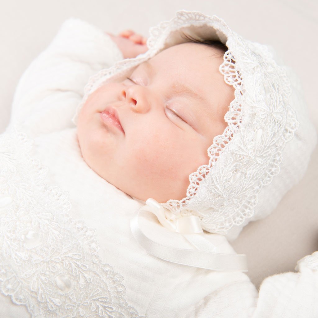 A peaceful newborn baby sleeping, dressed in a Madline Quilted Newborn Bonnet, lying on a soft beige background.