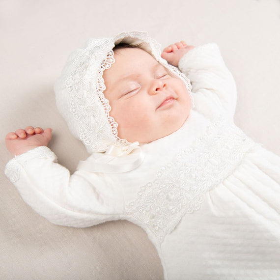 A newborn baby wearing the Madeline Quilted Newborn Romper sleeps peacefully with arms outstretched on a soft beige background.