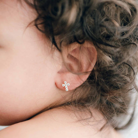 a close up image of a baby girl wearing jeweled cross earrings - gold